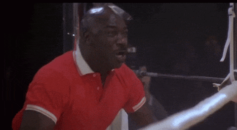 a man in a red shirt is sitting in a boxing ring .