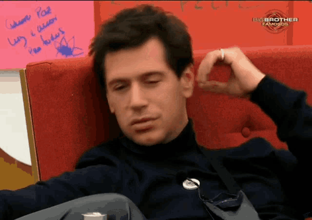 a man sits in a chair with his eyes closed and a big brother logo behind him