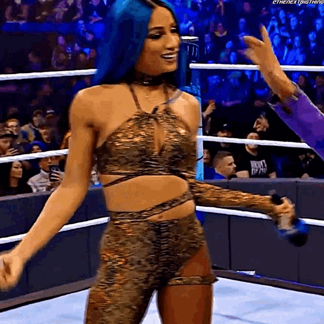 a woman with blue hair is dancing in a wrestling ring while holding a microphone .