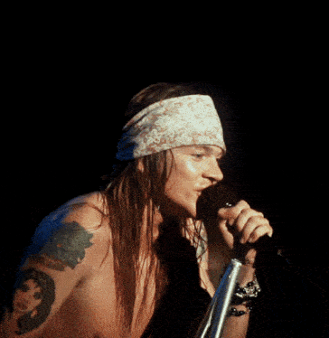 a shirtless man singing into a microphone with a tattoo on his arm