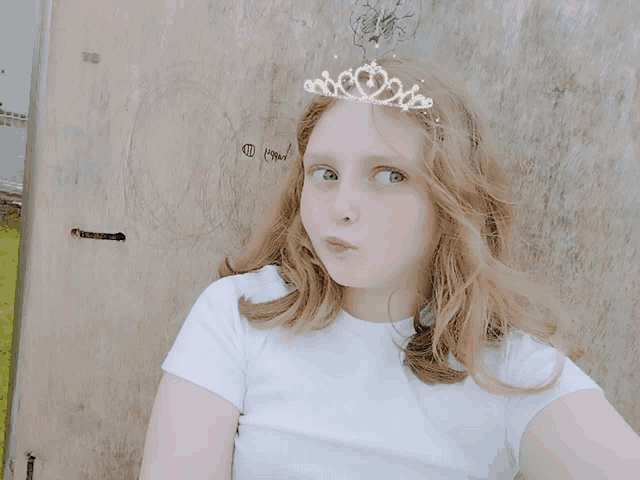 a young girl wearing a white shirt and a tiara on her head looks at the camera