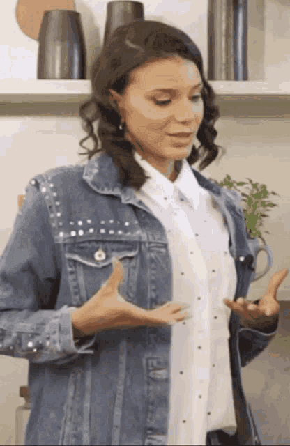 a woman wearing a white shirt and a denim jacket is giving a thumbs up