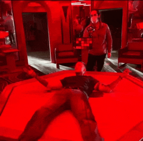 a man is laying on a bed in a room with red lights behind him .