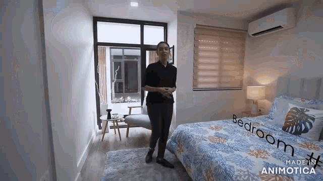 a woman is standing in a bedroom with a bed and a large window .
