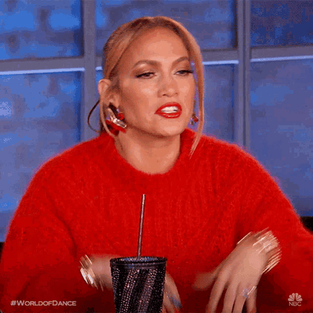 a woman in a red sweater is holding a black cup with a straw in her hand .