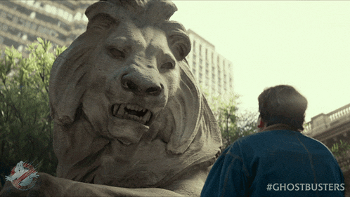a man standing in front of a statue of a lion with the hashtag #ghostbusters on the bottom