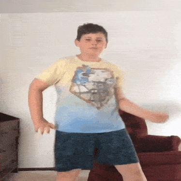 a young boy in a yellow shirt and blue shorts is dancing in a living room