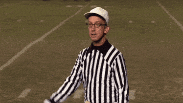 a referee wearing glasses and a striped shirt stands on a field