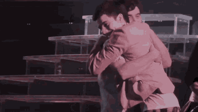 two men hugging each other in front of a staircase