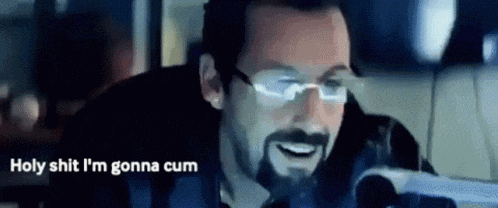 a man with glasses and a beard is smiling while looking at a computer screen .