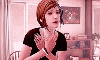 a woman is sitting at a table in a living room with her hands folded in front of her chest .