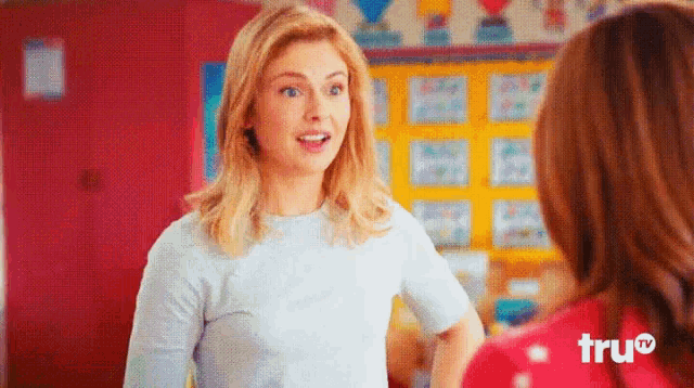 a woman in a white shirt is talking to another woman in a red shirt in front of a wall that says tru