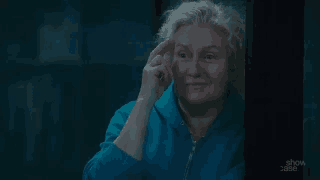 a woman in a blue hoodie is looking out a window with show case written on the bottom of the screen
