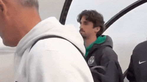 a man in a green jacket is standing next to another man in a white shirt .
