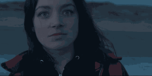a woman with dark hair and blue eyes looks at the camera