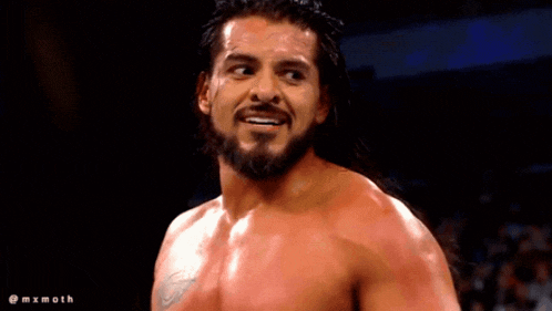 a shirtless wrestler with a tattoo on his chest stands in the dark