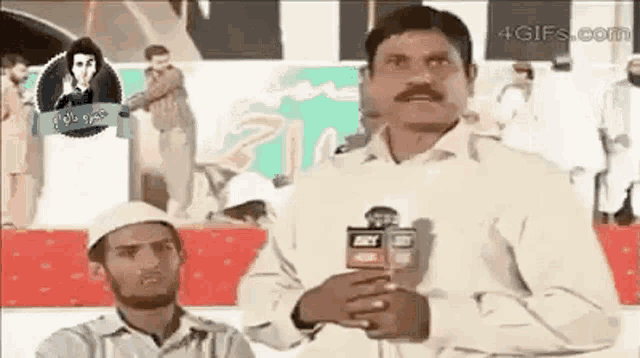 a man in a white shirt is holding a microphone while another man looks on .
