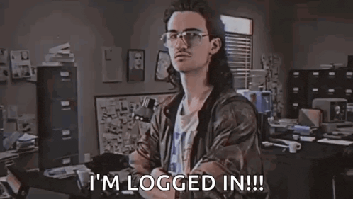a man with long hair and glasses is sitting at a desk in an office .