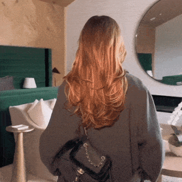 a woman with long red hair stands in front of a mirror