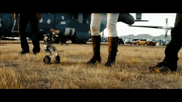 a group of people standing in a field with a helicopter in the background that has the letter j on it