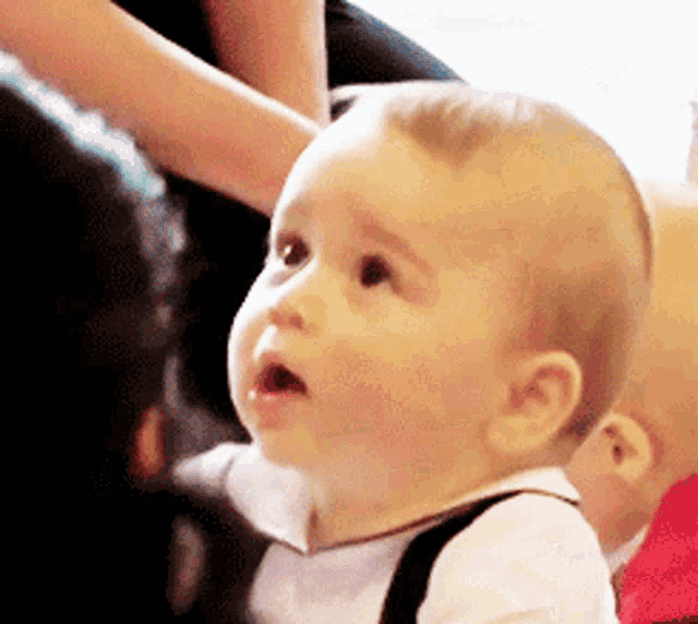 a baby wearing suspenders and a white shirt is looking up