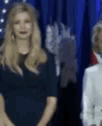 a woman in a black dress is standing next to a woman in a white coat in front of an american flag .