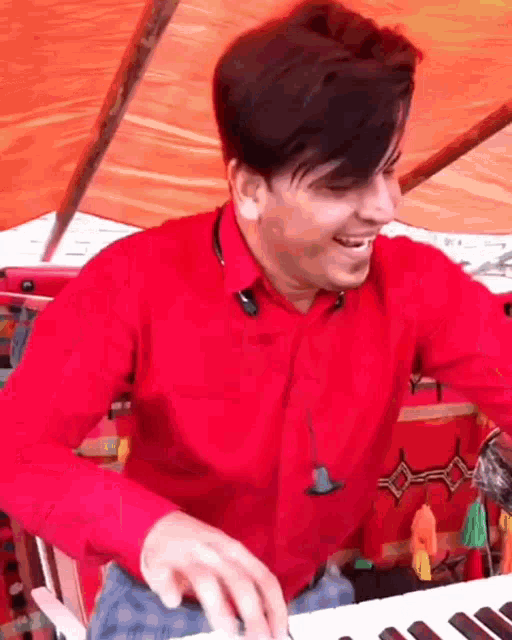 a man in a red shirt is smiling while playing a keyboard