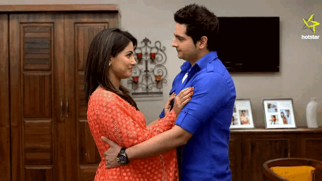 a man and a woman are hugging in a living room with a hotstar logo in the corner