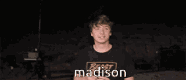 a young man wearing a madison t-shirt looks at the camera