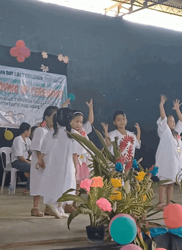 a group of children are dancing in front of a banner that says ' giving ceremony ' on it