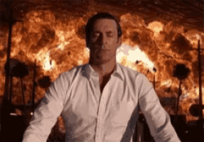 a man in a white shirt is standing in front of a large fire .