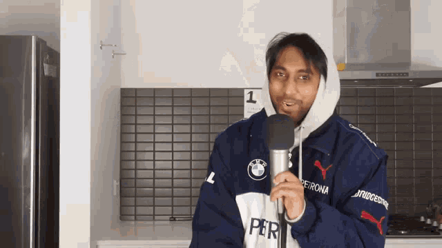a man wearing a bmw jacket is holding a microphone in a kitchen