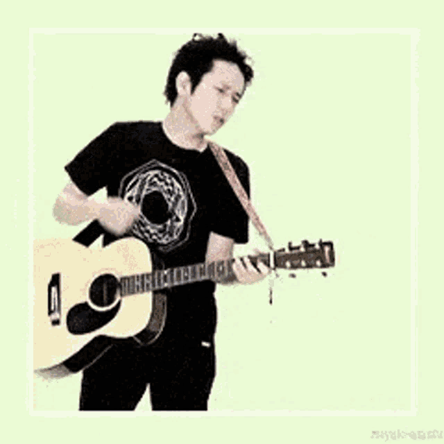 a young man in a black shirt is playing an acoustic guitar .