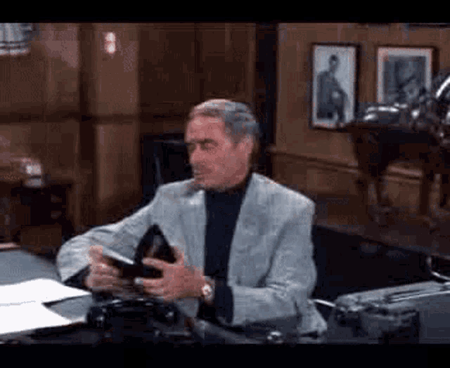 a man in a suit is sitting at a desk holding a wallet in his hands .