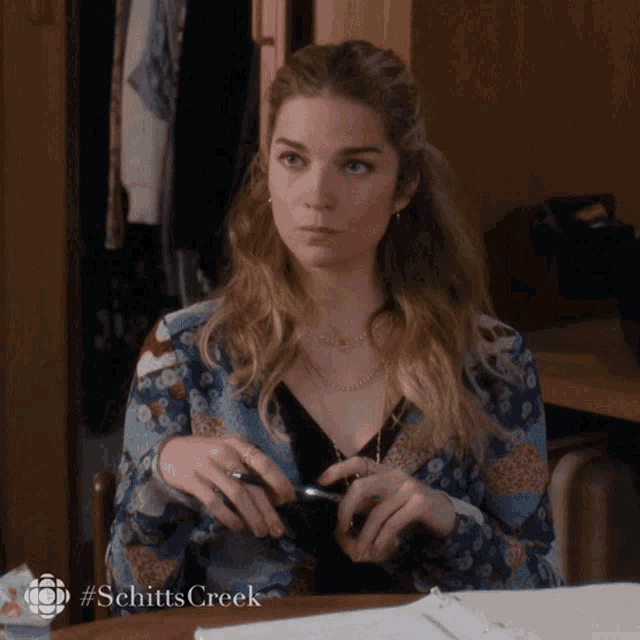 a woman sitting at a desk with the hashtag #schitts creek
