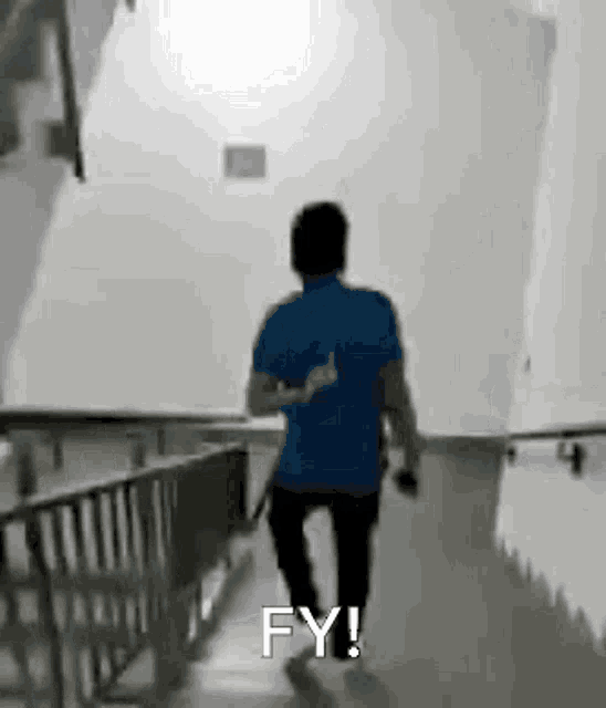 a man in a blue shirt is walking down a hallway with the words `` fy ! '' written on the bottom .