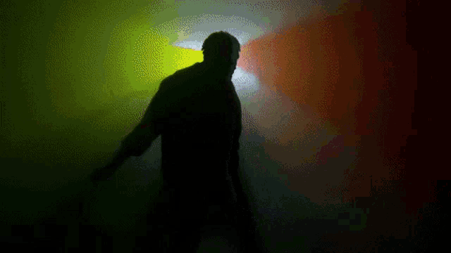 a silhouette of a man standing in front of a colorful light