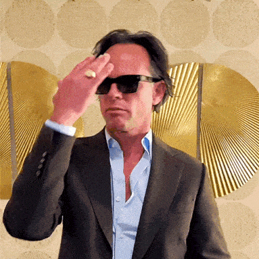 a man in a suit and sunglasses holds his hand to his head