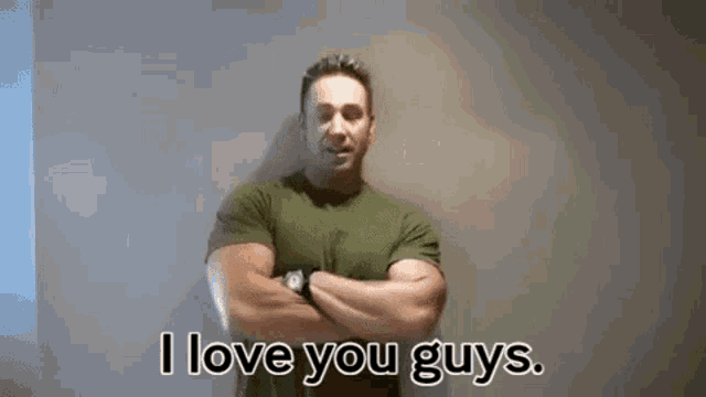 a man with his arms crossed is standing in front of a wall and saying `` i love you guys '' .