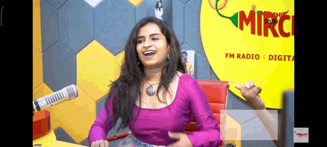 a woman in a pink top is laughing in front of a sign that says mirchi