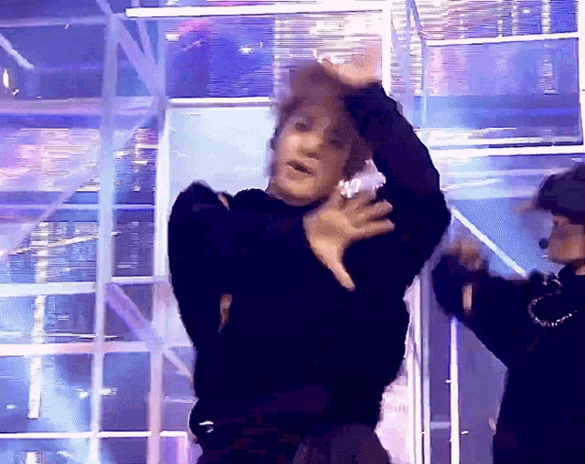 a man in a black sweater is dancing on a stage with his hands in the air