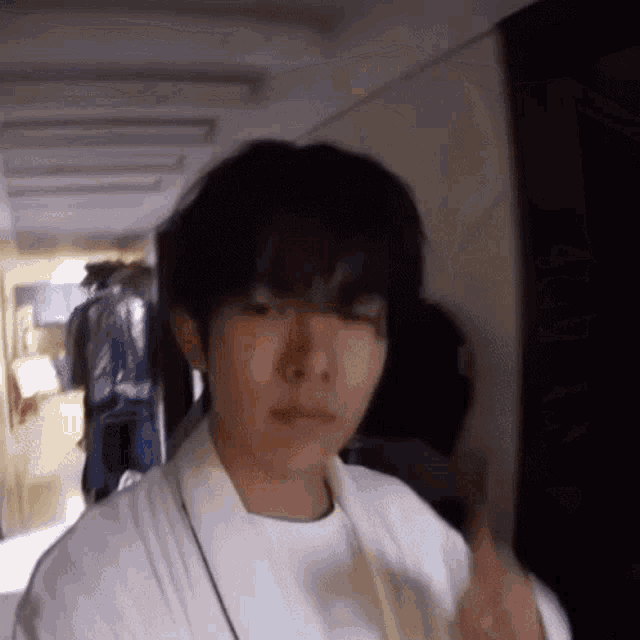 a young man in a white robe is standing in a hallway and making a funny face .