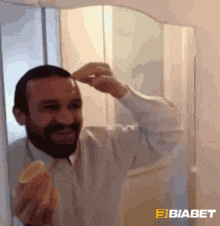 a man with a beard is looking at himself in a mirror while holding an orange slice