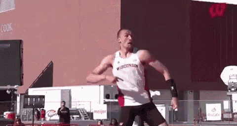 a man is jumping in the air while wearing a wisconsin shirt and black shorts .
