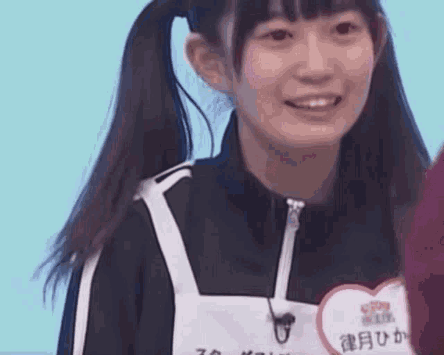 a young girl with pigtails is smiling and wearing a heart shaped tag .