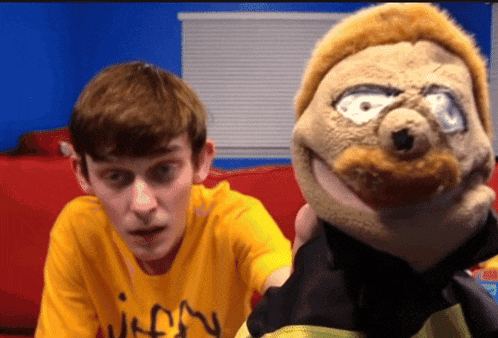 a man wearing a yellow shirt that says " wiffany " looks at a stuffed animal