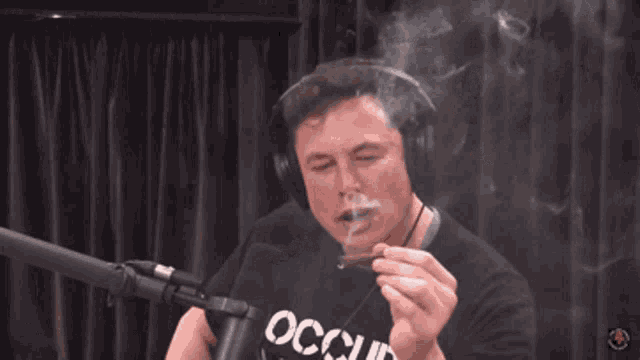 a man wearing headphones is smoking a cigarette while sitting in front of a microphone .
