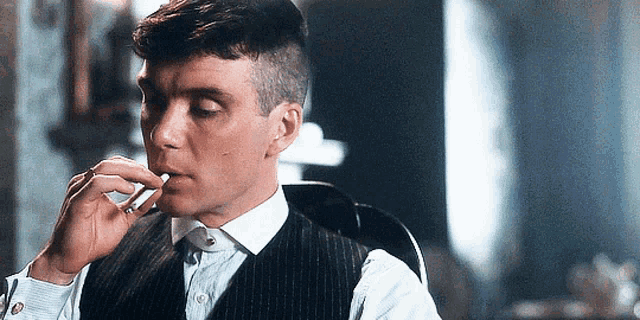 a man in a suit is smoking a cigarette while sitting in a chair .