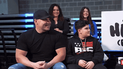 a man wearing a black shirt that says abc sits next to two other people