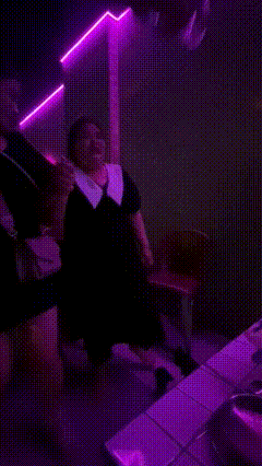 a woman in a black dress is sitting in a dark room under purple lights .